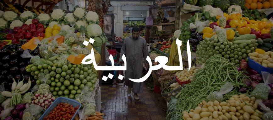 A man walking through a vegetable market, overlaid with Arabic script