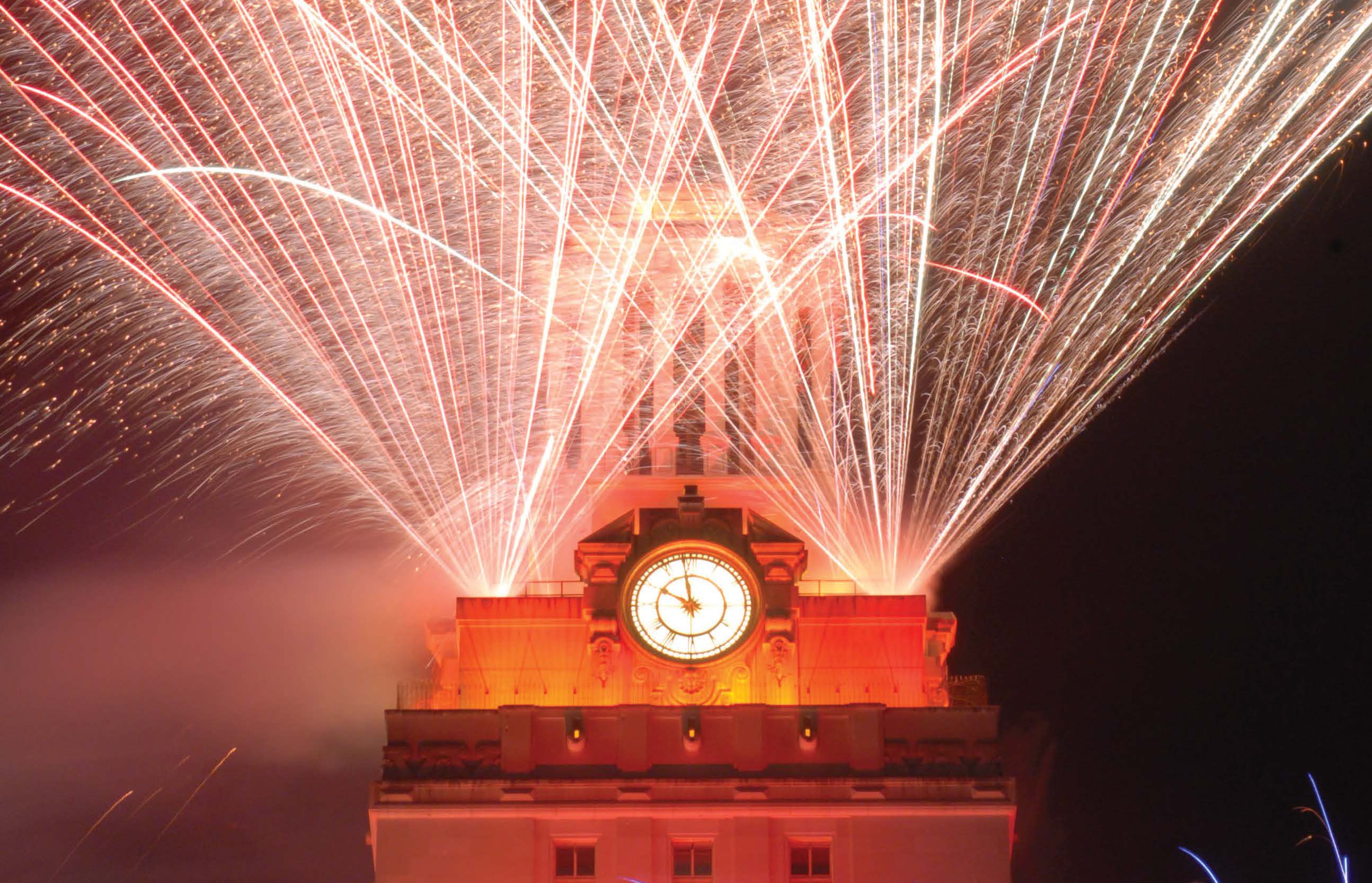 multiple fireworks light up the night sky behind the UT tower.