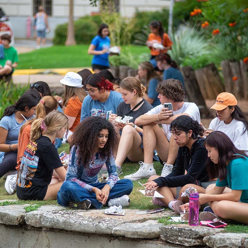 students sitting on the ground outside eating ice cream near the turtle pond