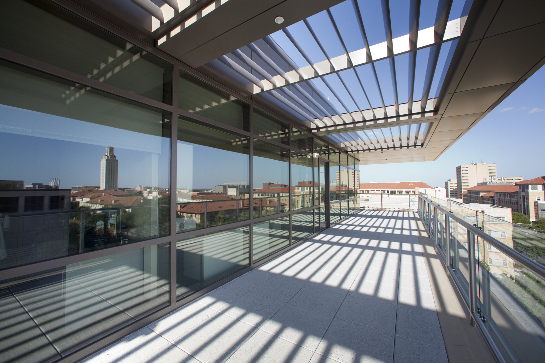 a view of campus rooftops and the tower reflected in the window of a outdoor balcony area