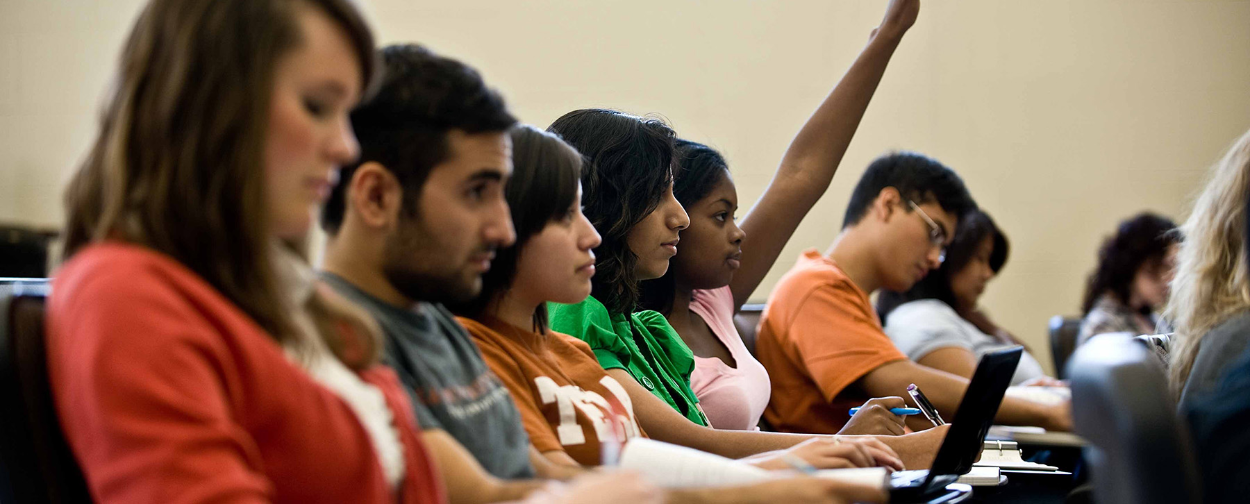 a row of students in a classroom listening to a lecture and taking notes